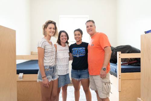 Students and parents smiling in residence hall room.